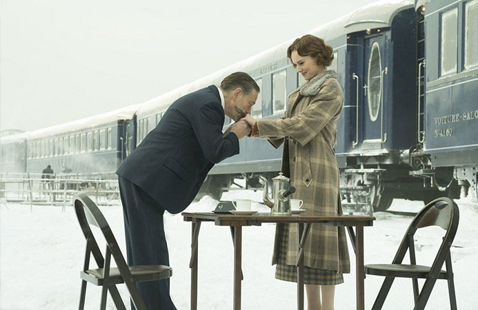 Snowy scene from the film Murder on the Orient Express with a couple having tree next to the train